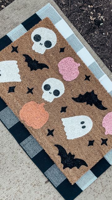 a halloween door mat on the ground with skulls and bats around it in black, pink, orange, and white