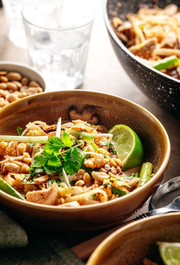 two bowls filled with food sitting on top of a table next to glasses and spoons