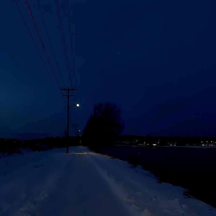 an empty road at night with power lines and telephone poles in the snow on either side