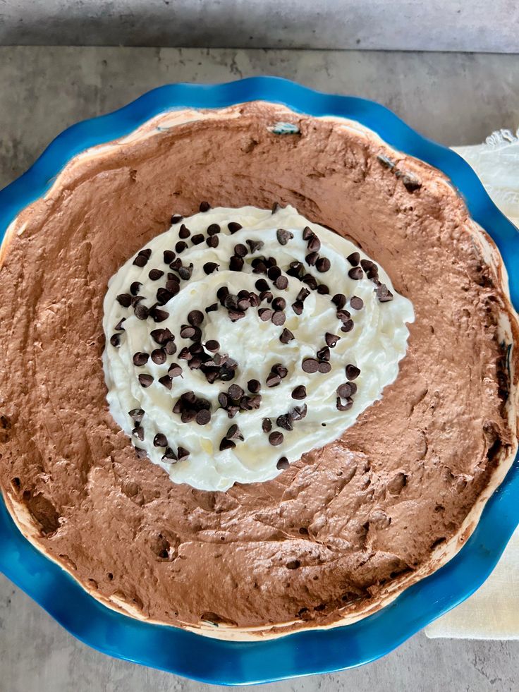 a chocolate pie with whipped cream and chocolate chips on top, sitting on a blue plate