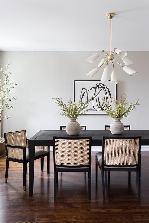 a dining room table with four chairs and two plants in vases on the table