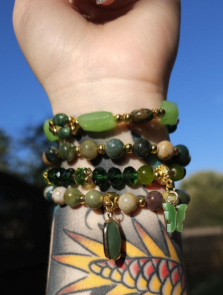 This is a handmade, natural crystal bracelet stack. Each bracelet is approximately 7 inches in length around and made with stretch wire. This version features natural green jasper, serpentine and Czech crystal with gold plating. It has two pendants: a green butterfly and a green aventurine cabochon. This is a 4 piece set! This is a handmade item and may be subject to some slight flaws. No two items will be the same. Handmade Green Aventurine Crystal Bracelet, Bohemian Green Agate Crystal Bracelet, Green Wire Wrapped Spiritual Bracelets, Green Spiritual Wire Wrapped Bracelets, Spiritual Green Wire Wrapped Bracelets, Green Agate Crystal Bracelet With Gemstone Beads, Green Aventurine Stretch Bracelet With Natural Stones, Green Aventurine Crystal Bracelet With Natural Stones, Adjustable Green Stretch Bracelet With Natural Stones