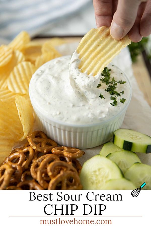 a person dipping some food into a bowl with chips and cucumbers around it