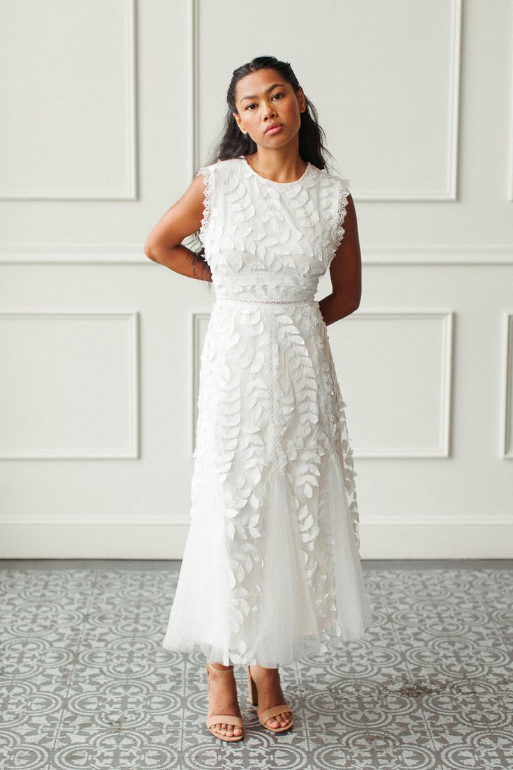 a woman wearing a white dress standing in front of a wall