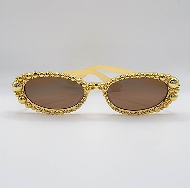 Oval sunglasses with mock goal pearl detail. These striking sunglasses are one-of-a-kind, with each pearl placed by hand. They make the perfect party, wedding, bridal party, festival or sunday in the sun fashion accessory. Our items are made to be exclusive and not mass-produced, meaning you are purchasing the exact pair provided in the picture so you can be sure you will love your new shades. Frame colour: Gold pearls on a translucent gold frame Lens colour: Gold Shape: Oval Original frame bran Glamorous Gold Sunglasses For Party, Glamorous Gold Party Sunglasses, Glamorous Gold Sunglasses For Summer, Gold Mirrored Sunglasses For Party, Gold Mirrored Lenses Sunglasses For Party, Gold Party Sunglasses, Gold Sunglasses For Summer Festival, Gold Tinted Sunglasses For Festival, Elegant Summer Wedding Sunglasses