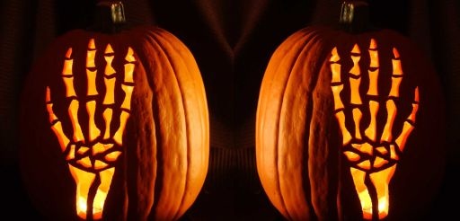 two carved pumpkins with hands on them in the dark, one is lit up