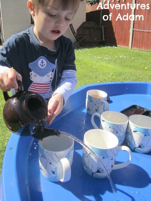 a young boy is pouring water from a pitcher into cups on a blue table outside