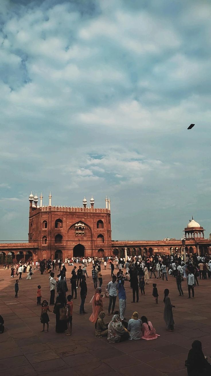 many people are standing around in front of a large building with a bird flying overhead