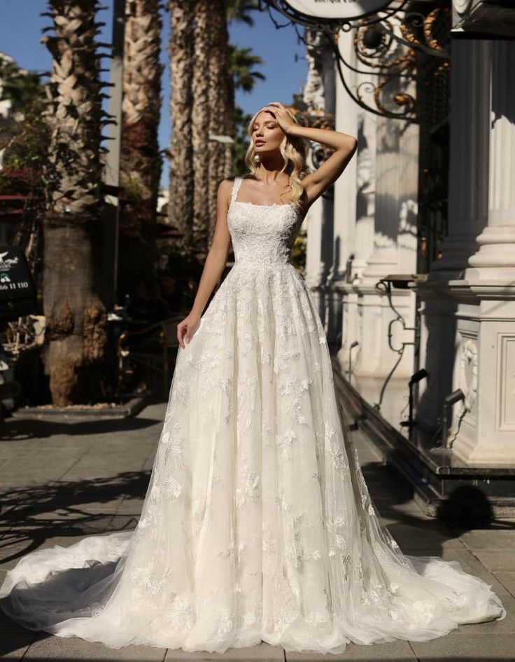 a woman in a wedding dress standing on the sidewalk with her hand on her head