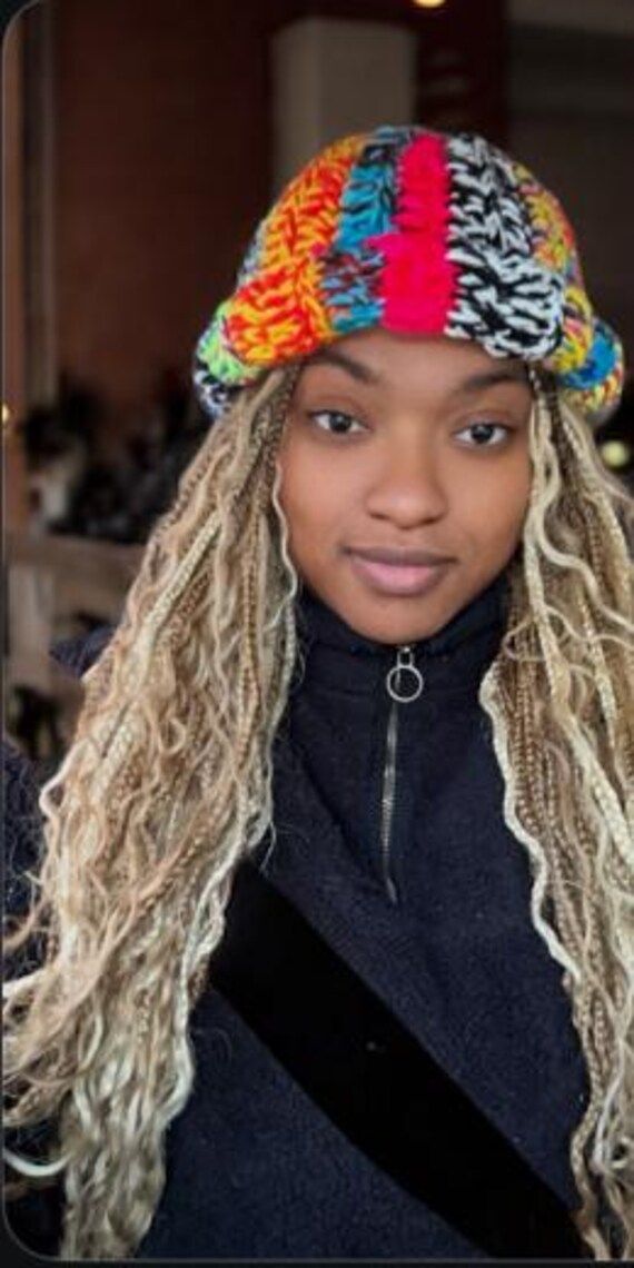 a woman with long blonde hair wearing a multicolored knitted beanie hat