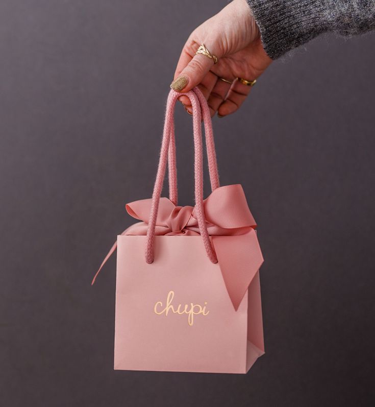 a person holding a pink shopping bag with the word chopi on it and a bow