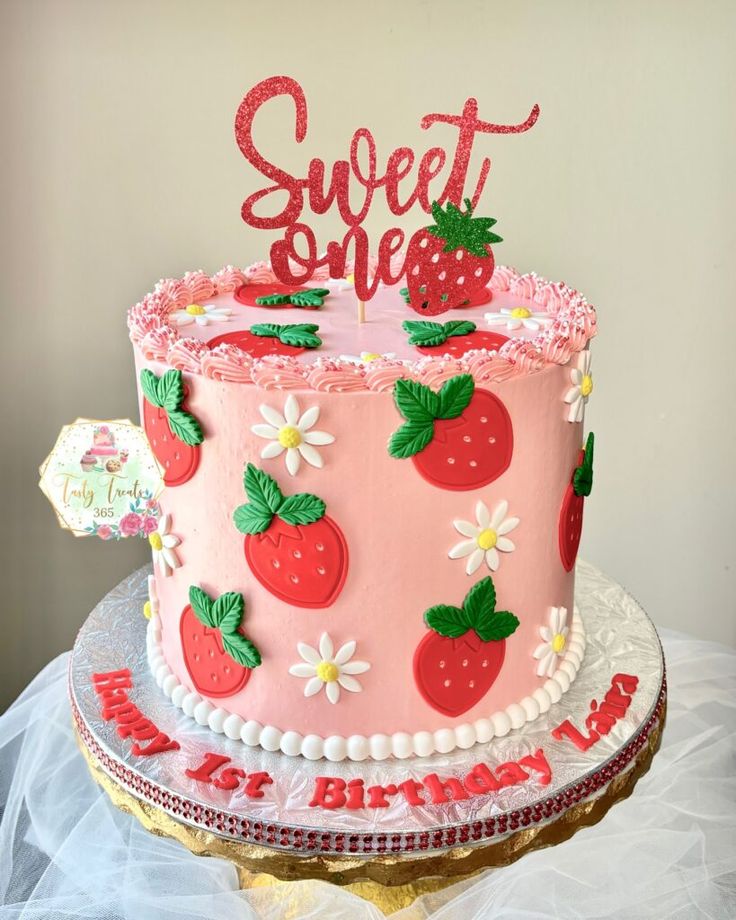 a pink cake decorated with strawberries and the words sweet one