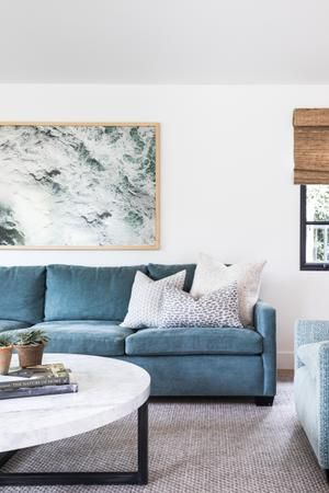 a living room filled with blue couches and a white coffee table in front of a painting