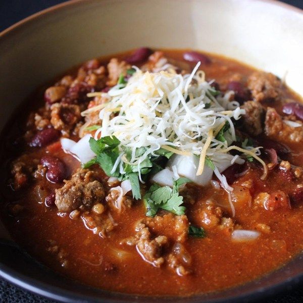 a white bowl filled with chili and cheese on top of a black countertop next to a spoon