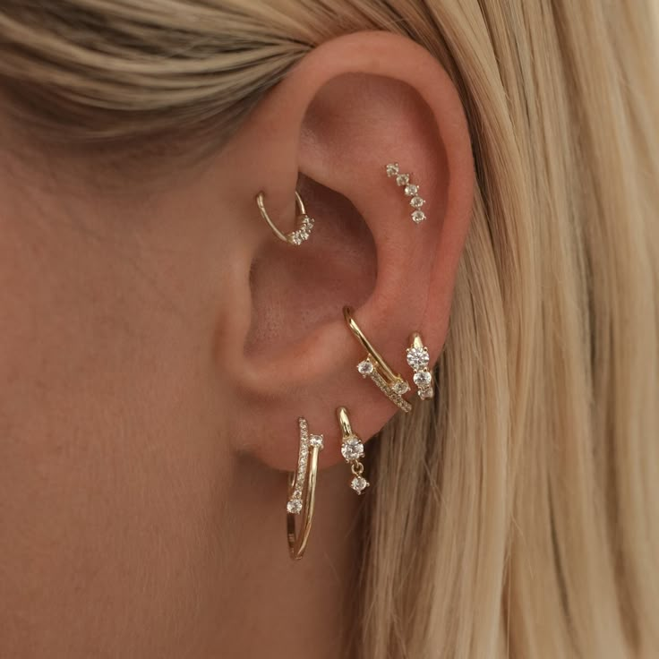 a woman wearing three different types of ear piercings on her left ear and the other one is gold