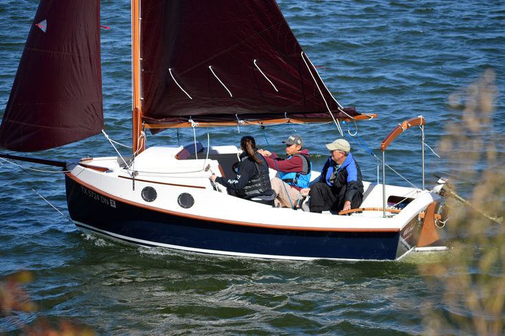 three people on a small sailboat in the water with one person sitting at the helm