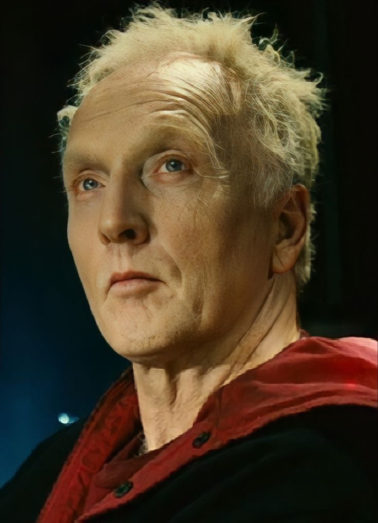 an older man with blonde hair wearing a red shirt and black jacket looking off to the side