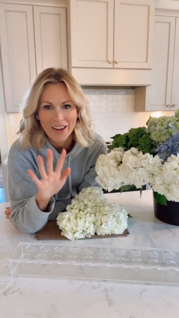 a woman sitting at a counter with flowers in front of her and making the peace sign