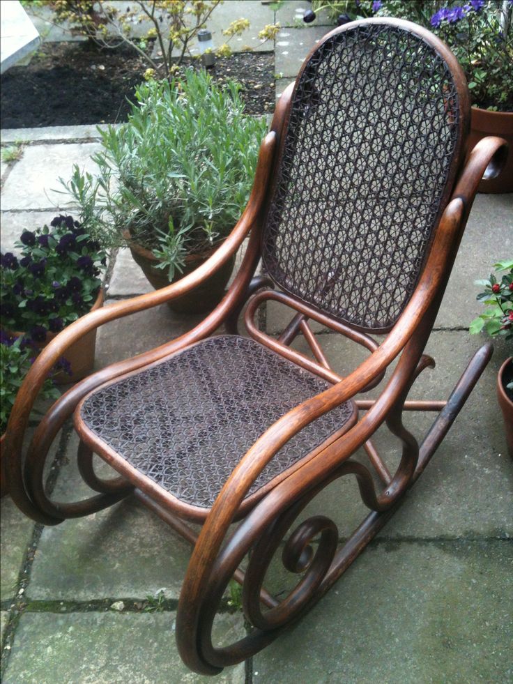 a wooden rocking chair sitting on top of a stone floor next to potted plants