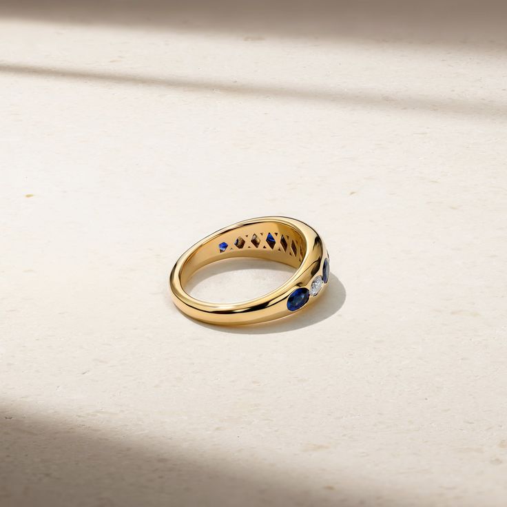 a yellow gold ring with blue stones on the outside and inside, sitting on a white surface