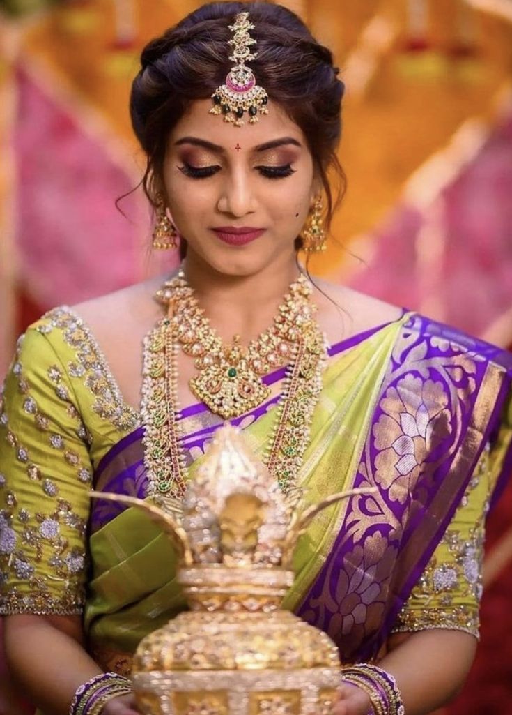 a woman in a green and purple sari holding a golden vase with jewels on it