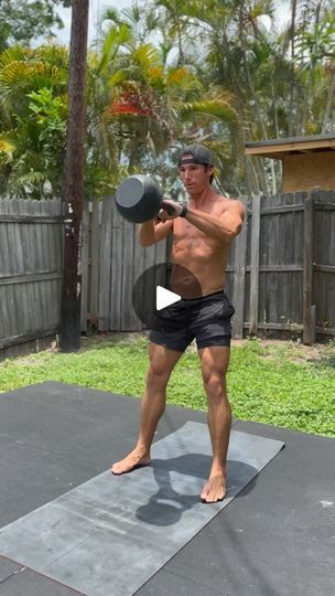 a shirtless man holding a dumbbell while standing on a mat