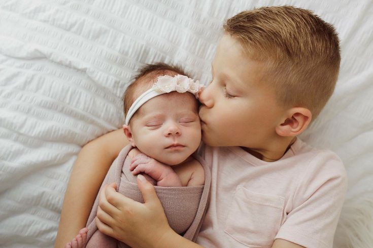 a young boy kissing his newborn sister on the cheek