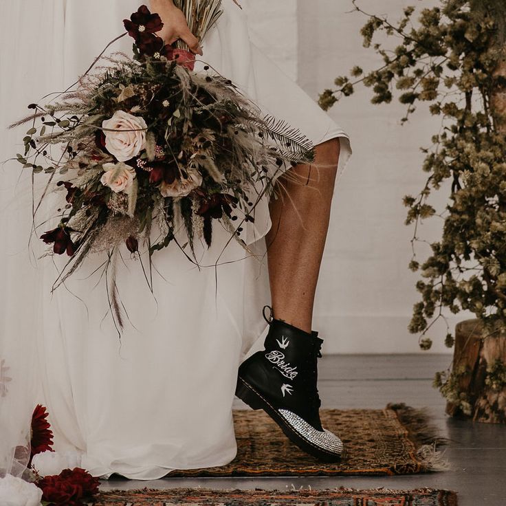 a woman in black boots is holding a bouquet and standing on a rug with flowers