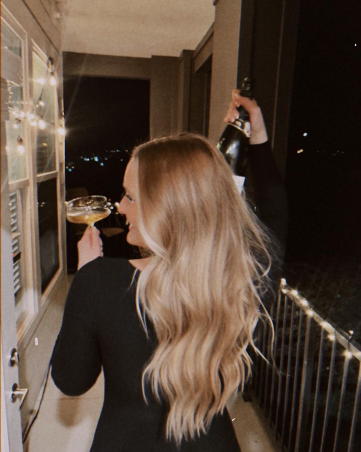 a woman standing on a balcony drinking from a wine glass in front of a window