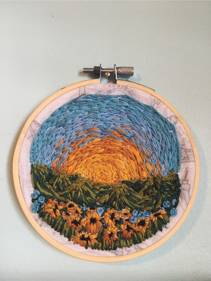 an embroidery project with sunflowers in the center and blue sky behind it on a white wall