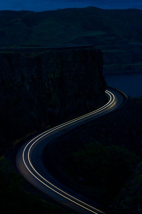 a long exposure shot of a road going through the mountains at night with lights on