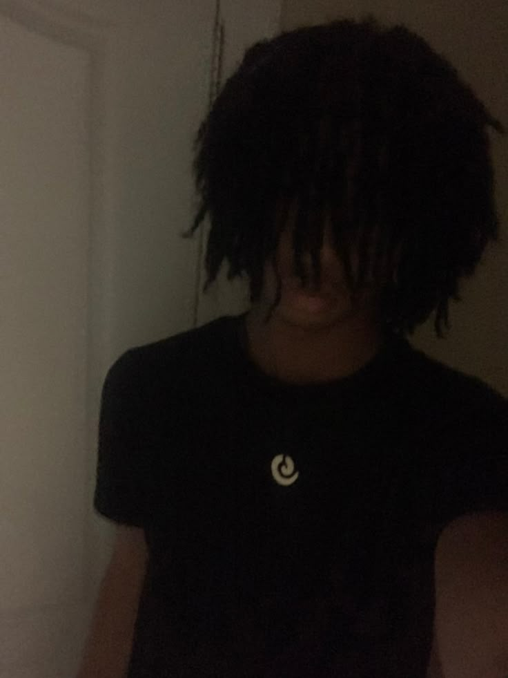 a man with dreadlocks standing in front of a door wearing a black shirt