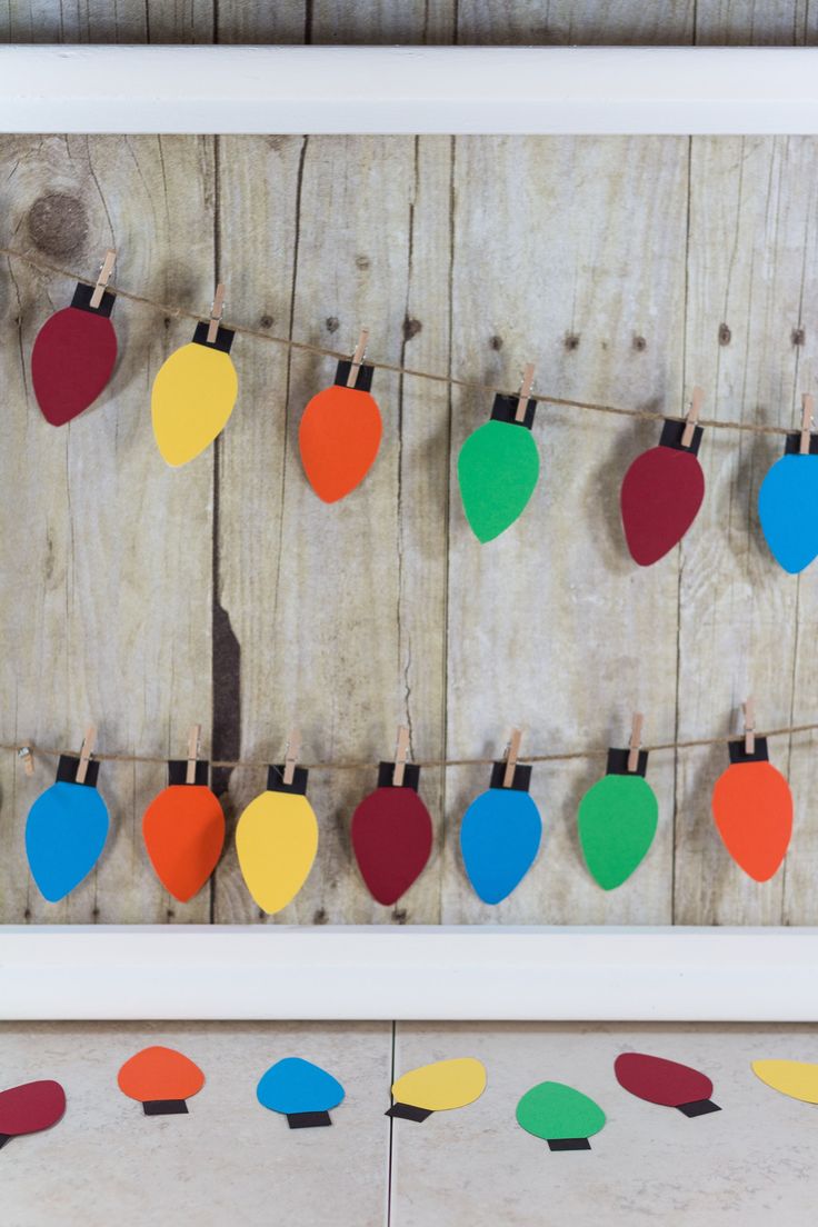 colorful christmas lights hanging on clothes pins in front of a white frame with wood planks