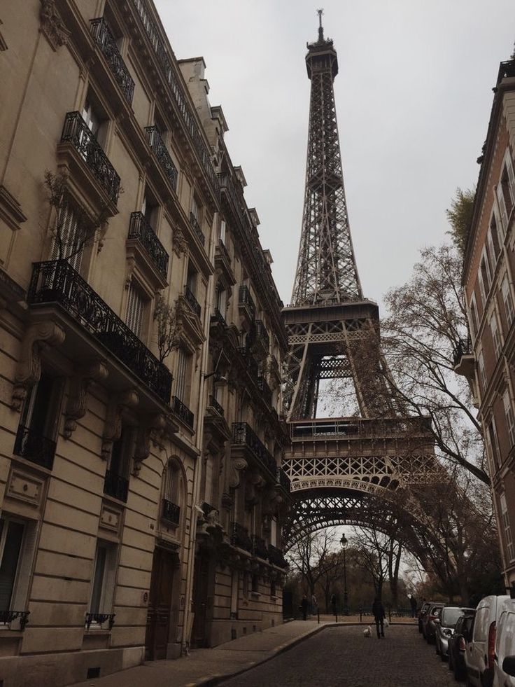 the eiffel tower towering over an alley way in paris, with cars parked on both sides