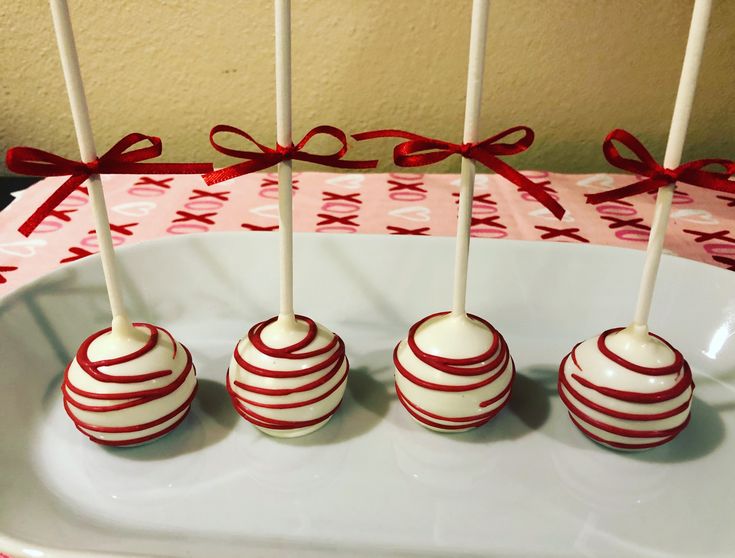 four cake pops with red and white stripes are on a plate next to a gift box