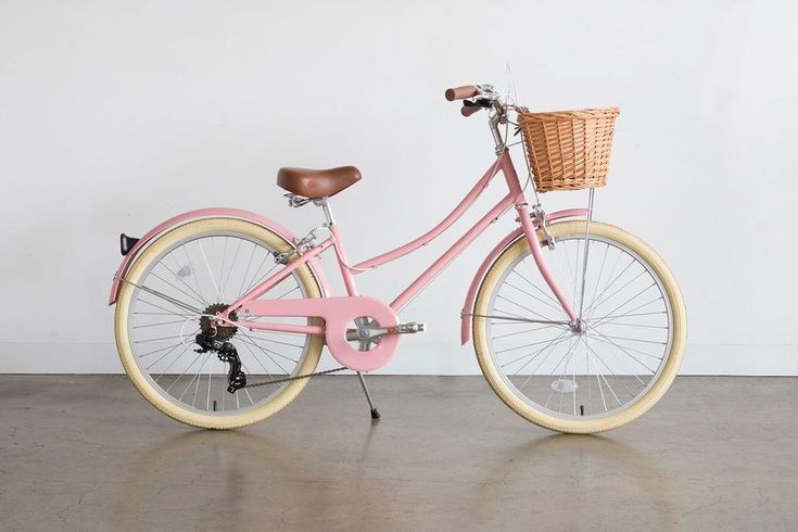 a pink bicycle with a basket on the front and back wheel, parked against a white wall