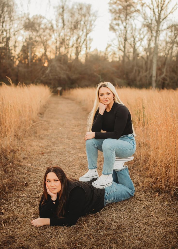 two women sitting on top of each other in the middle of a field with tall grass