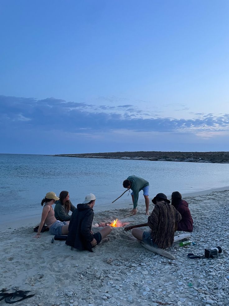 several people are sitting on the beach and one person is lighting a candle in the sand