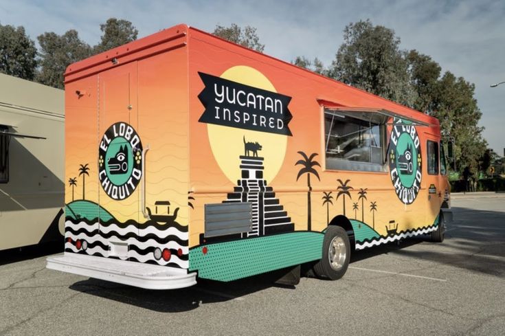 an orange and green food truck parked in a parking lot next to another vehicle on the road