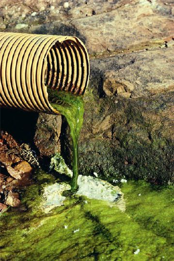 green liquid pouring out of a wooden barrel into the ground with rocks in the background