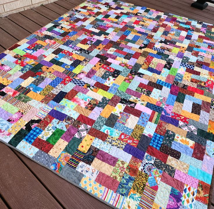 a multicolored patchwork quilt on a wooden deck