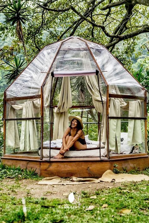 a woman sitting on top of a bed under a canopy in the grass with trees