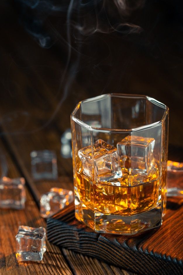 a glass filled with ice sitting on top of a wooden table