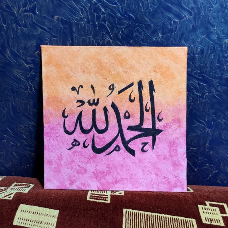 a painting with arabic writing on it sitting on top of a brown and pink blanket