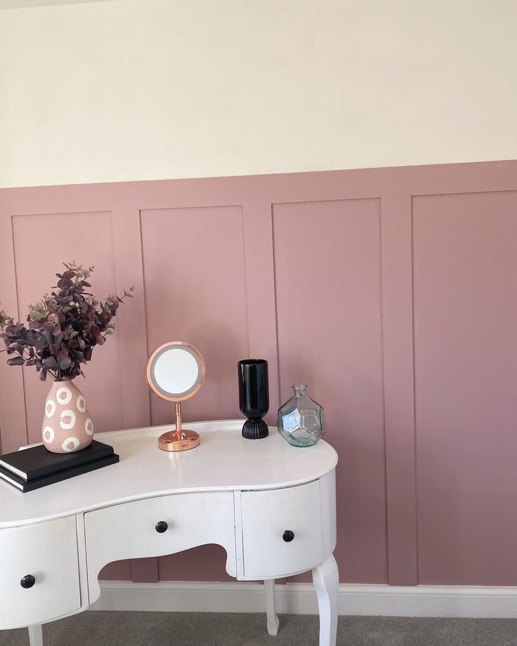 a white desk with a mirror and vase on it in front of a pink wall