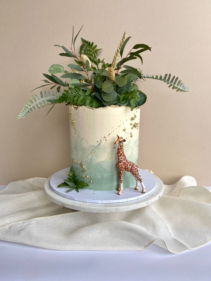 a cake with a giraffe decoration on it and plants in the top tier