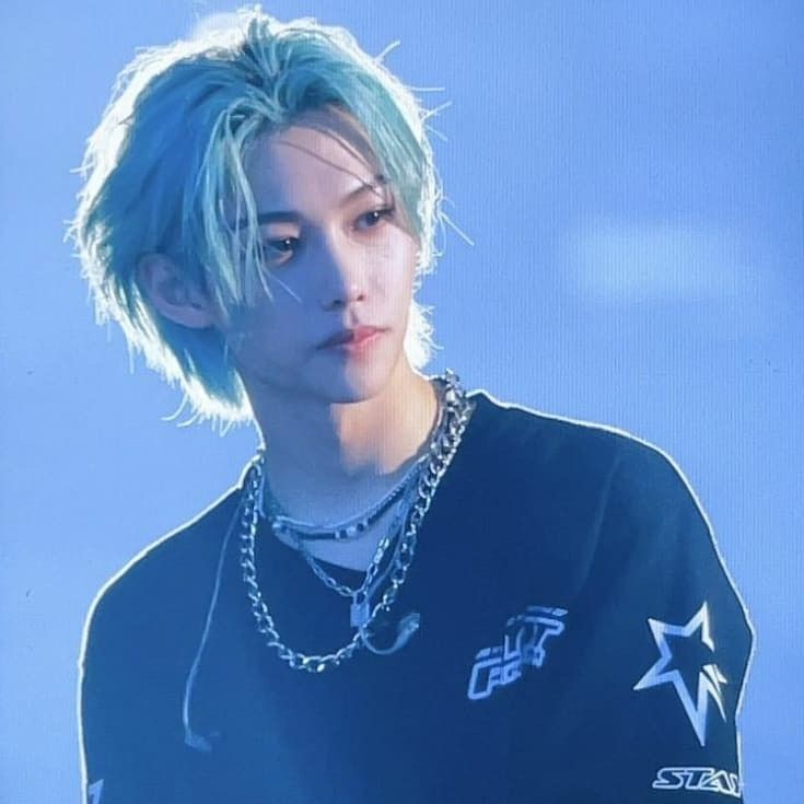 a young man with blue hair wearing a black t - shirt and silver necklaces