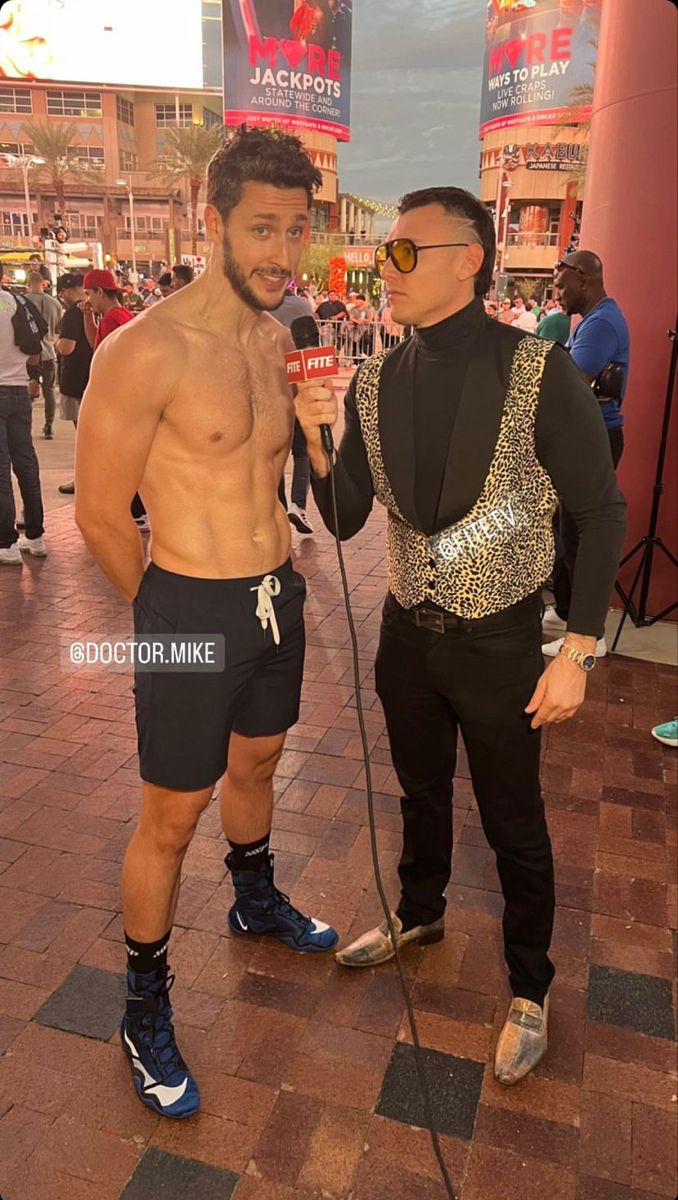 two shirtless men standing next to each other on a brick floor in front of a building