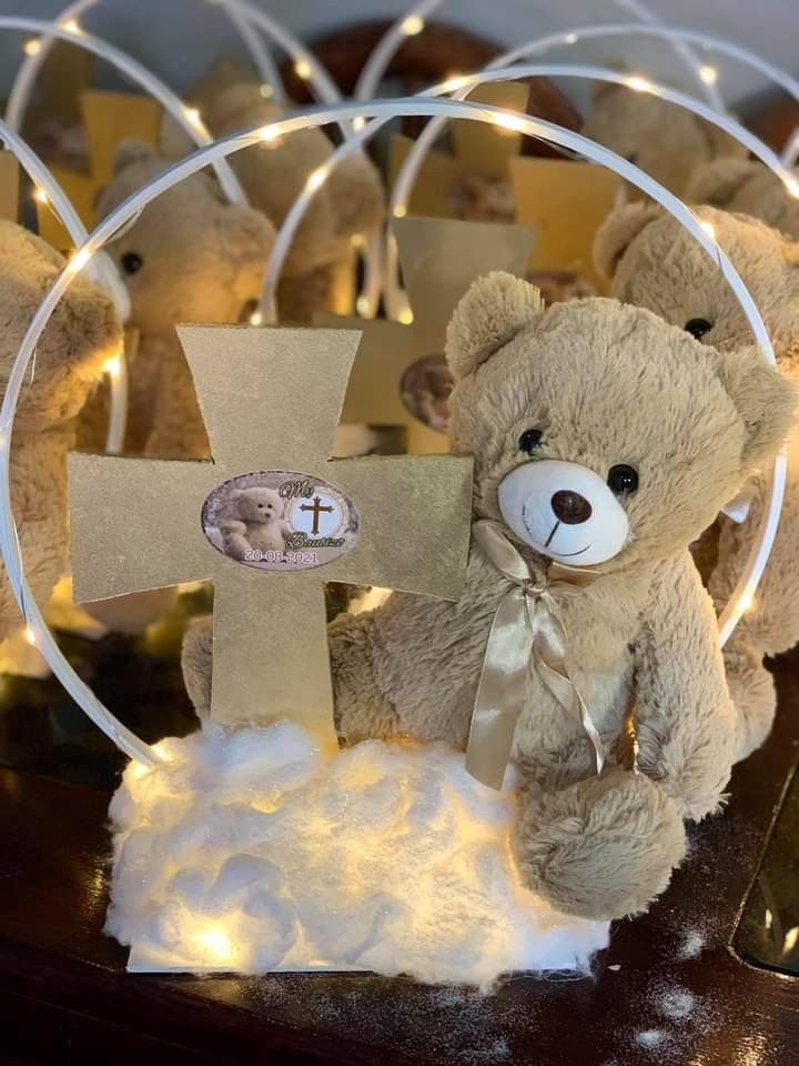 a teddy bear sitting in front of a cross on a table with lights around it