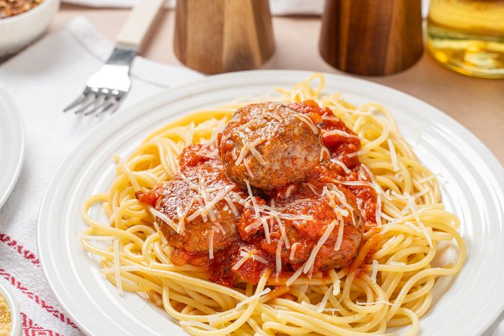 spaghetti and meatballs on a plate with parmesan cheese, breadcrumbs